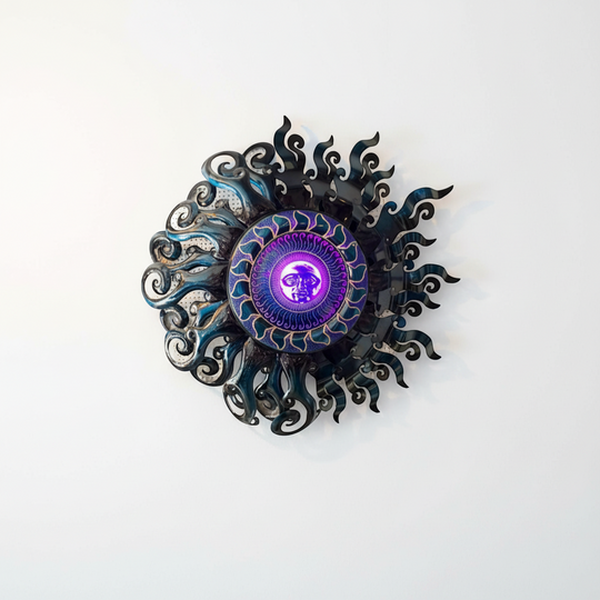 The Talavera Hub Giant Sun Wall Art, handmade Mexican metalwork with a radiant sun face and swirling rays, features a built-in light fixture. Blue and metallic.