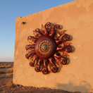 The Talavera Hub Giant Sun Wall Art, handmade metalwork with a face and red swirling rays, includes light fixture.