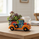 The Talavera Hub hand-painted ceramic car planter. Small orange truck with colorful floral designs and blue trim.