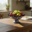 The Talavera Hub hand-painted blue and white ceramic fruit bowl filled with apples, grapes, cherries, kiwi, and lemon.