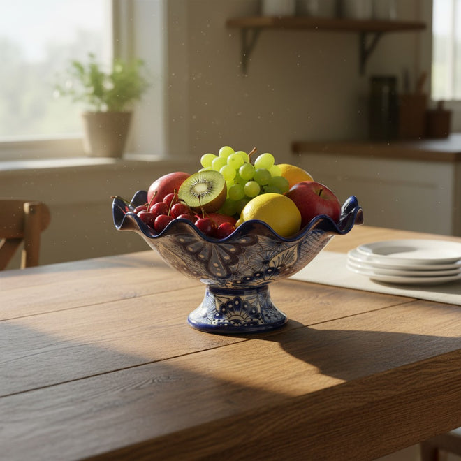 The Talavera Hub hand-painted blue and white ceramic fruit bowl filled with apples, grapes, cherries, kiwi, and lemon.