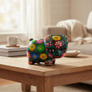 The Talavera Hub handmade ceramic piggy bank featuring vibrant hand-painted floral patterns on a black background.