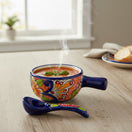 The Talavera Hub hand-painted ceramic soup bowl with matching spoon filled with steaming tomato soup on a wooden table
