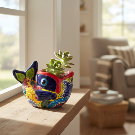 The Talavera Hub hand-painted ceramic fish planter in vibrant red, yellow, and blue with floral motifs on a windowsill.