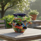The Talavera Hub hand-painted Mexican ceramic strawberry planter with vibrant floral patterns on a wooden patio table.