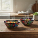 Two The Talavera Hub handmade Mexican ceramic soup bowls with vibrant floral patterns on a rustic wooden kitchen table.