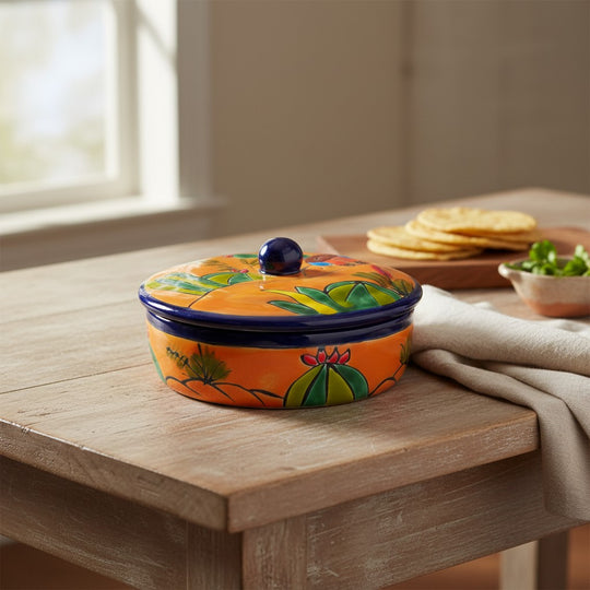 The Talavera Hub handmade orange ceramic tortilla warmer with colorful cactus and floral Talavera patterns and a blue knob.