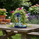The Talavera Hub hand-painted Mexican boot flower pot with butterfly and floral patterns on a wooden garden table.