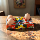 The Talavera Hub hand-painted ceramic egg holder with floral motifs in red, yellow, blue, and green.