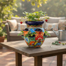 The Talavera Hub hand-painted Mexican ceramic strawberry planter with vibrant floral patterns on a wooden patio table.