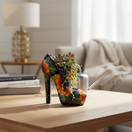 The Talavera Hub handmade ceramic high heel statue, hand-painted with vibrant orange flowers and green leaves on a dark blue base.