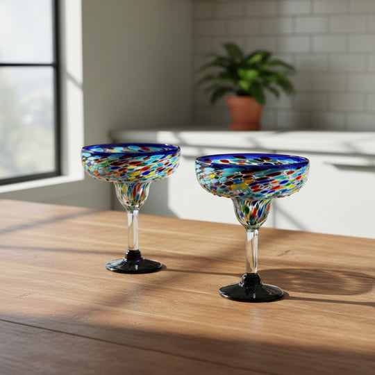The Talavera Hub Mexican hand-blown margarita glasses with blue confetti rock design. Clear glass with colorful flecks and dark bases.