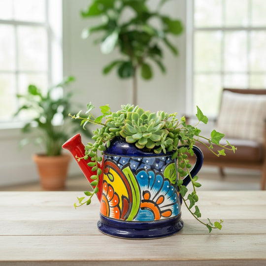 The Talavera Hub hand-painted blue ceramic watering can planter with red spout and vibrant floral designs.