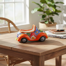 The Talavera Hub orange ceramic car planter with colorful hand-painted floral Talavera designs and black wheels.