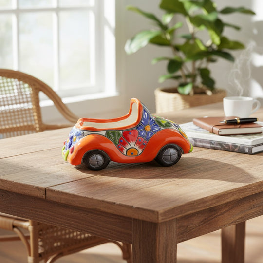 The Talavera Hub orange ceramic car planter with colorful hand-painted floral Talavera designs and black wheels.