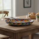 The Talavera Hub oval ceramic serving platter with vibrant hand-painted floral motifs and a cobalt blue rim on a table.