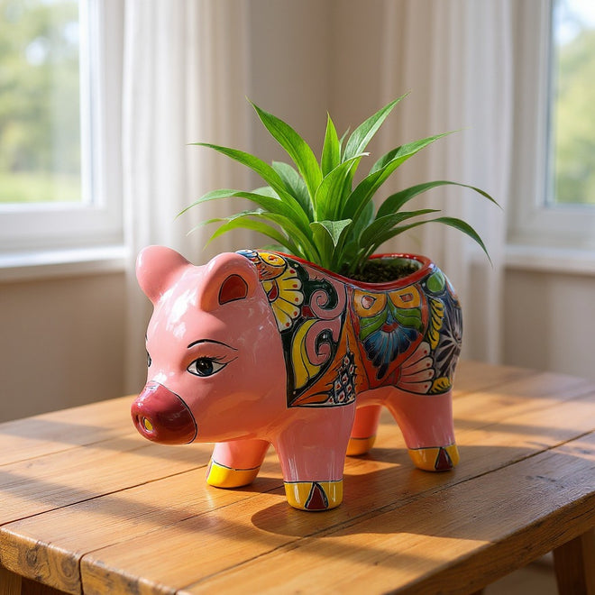 The Talavera Hub pink ceramic pig planter with hand-painted Mexican floral folk art patterns holding a green plant.