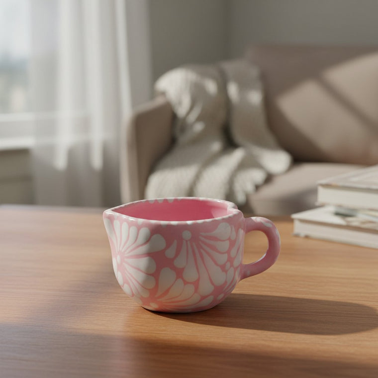 The Talavera Hub hand-painted pink ceramic heart-shaped mug with white floral patterns on a wooden table.