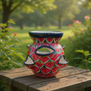 The Talavera Hub handmade red ceramic strawberry planter with peacock feather pattern on a wooden garden table.