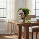 The Talavera Hub hand-painted ceramic Day of the Dead skull face planter with colorful floral designs and black striped neck.