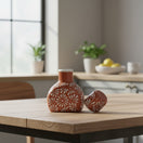 The Talavera Hub terracotta water carafe and cup set with hand-painted white floral motifs on a wooden kitchen table.