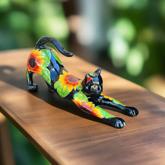 The Talavera Hub black ceramic cat statue with hand-painted sunflowers and green leaves, in a stretching pose.