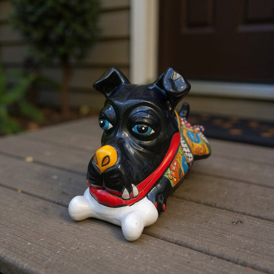 The Talavera Hub handpainted black ceramic dog decor with blue eyes, yellow nose, red collar, and bone in mouth.