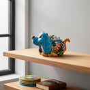 The Talavera Hub blue ceramic dog planter with hand-painted floral details and orange accents, holding a small green plant.