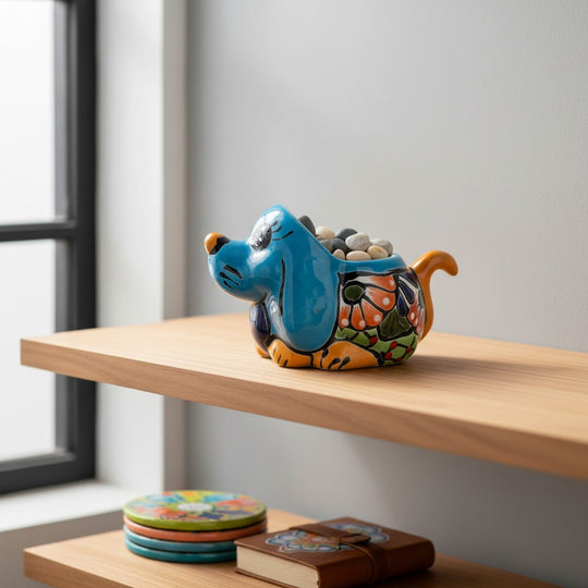 The Talavera Hub blue ceramic dog planter with hand-painted floral details and orange accents, holding a small green plant.