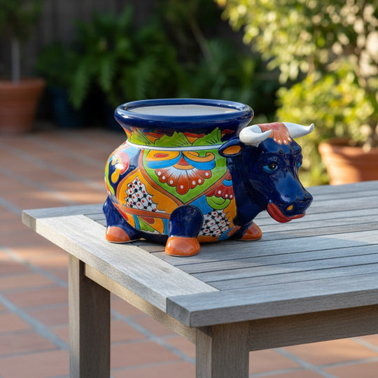 The Talavera Hub cobalt blue ceramic bull planter with vibrant floral patterns in orange, green, and yellow. Hand-painted Mexican pottery.