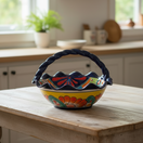 The Talavera Hub colorful hand-painted ceramic fruit basket with a braided blue handle and floral designs.