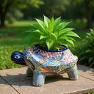The Talavera Hub hand-painted ceramic turtle planter with colorful floral and geometric designs. Features a dark blue rim and grey legs.