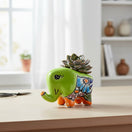 The Talavera Hub hand-painted ceramic elephant planter in lime green with colorful floral details and orange accents.
