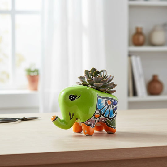 The Talavera Hub hand-painted ceramic elephant planter in lime green with colorful floral details and orange accents.