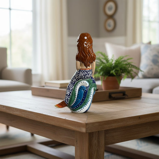 The Talavera Hub hand-painted ceramic mermaid figurine with floral tail, holding a yellow fish, resting on blue and green waves.