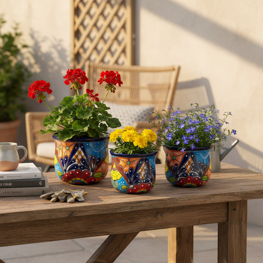 The Talavera Hub set of 3 colorful hand-painted ceramic flower pots with floral designs and blue rims.