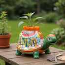The Talavera Hub medium hand-painted ceramic turtle planter with vibrant floral and bow details. Features a green head and orange rim.