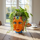 The Talavera Hub hand-painted Talavera face planter, orange ceramic with colorful headdress and blue base.