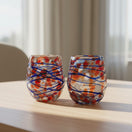 The Talavera Hub hand-blown stemless wine glasses with orange, red, and blue swirl pattern and blue web overlay.
